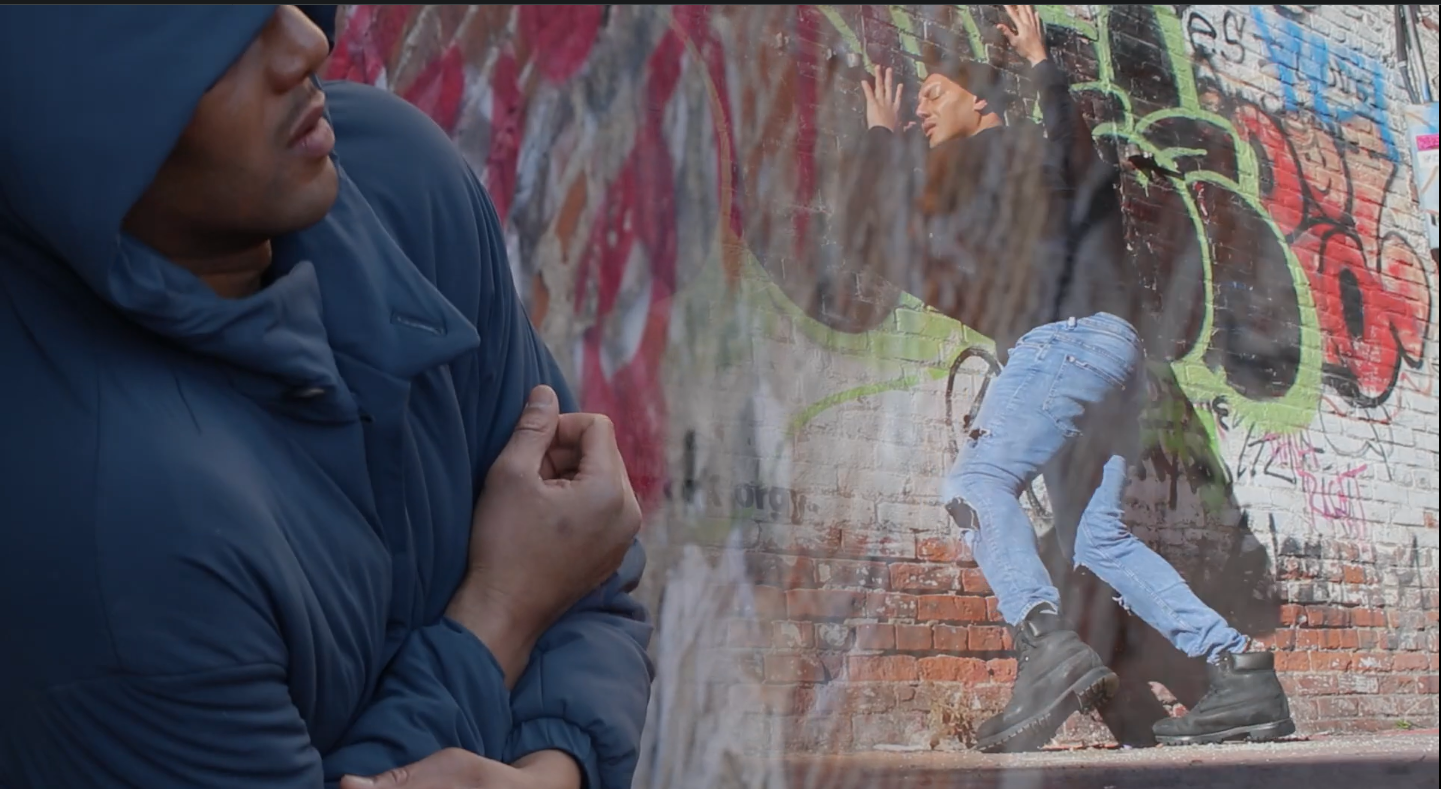 Darius Gray II dancing in front graffti on a brick wall.