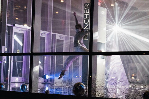 Dancer performing behind windows, surrounded by colored lights