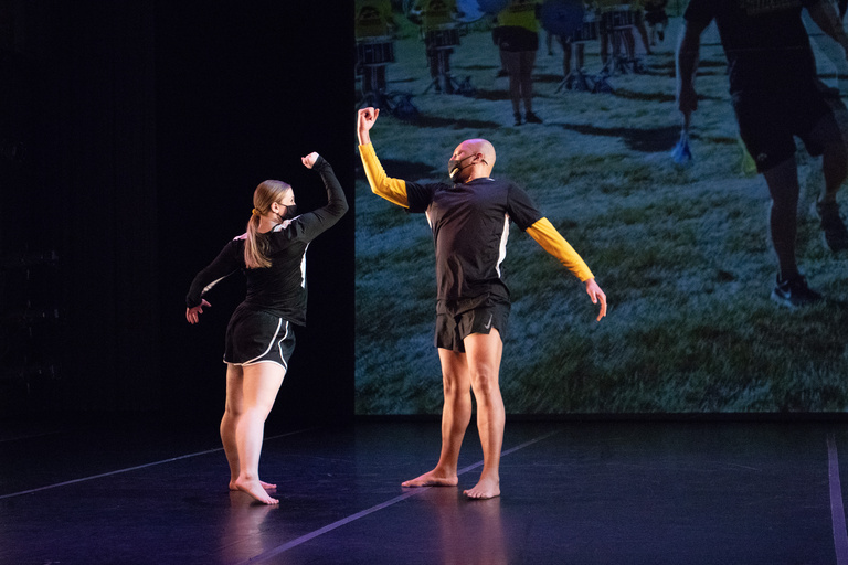 Two dancers facing each other with arms flexed and hands in fists