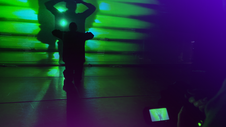 Dancer in performance being recorded by video camera.