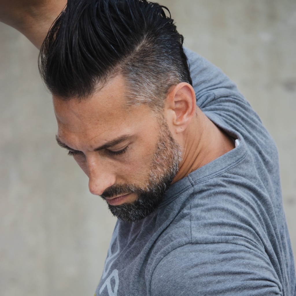 A close-up of Todd Rhoades mid-dance move. His body is facing the left, while his head is looking down and off-center from the camera.