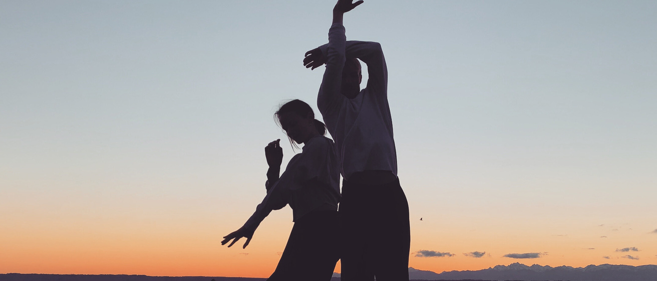 two dancers silhouetted against a sunset, on a beach