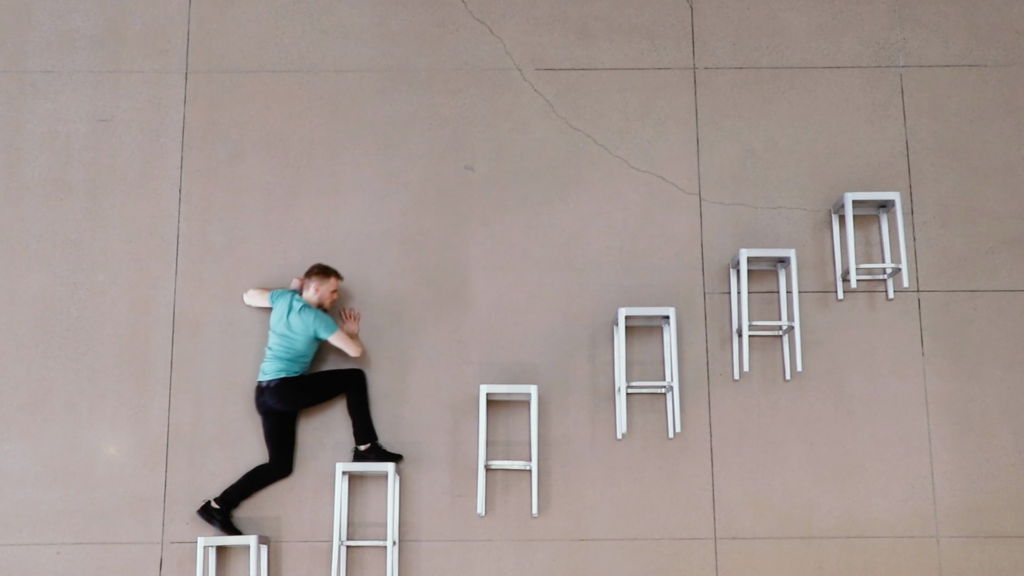 dancer walking on stools affixed to a large wall