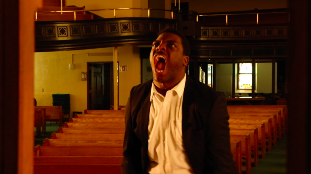 A man standing in a church, with his mouth open as if he is yelling