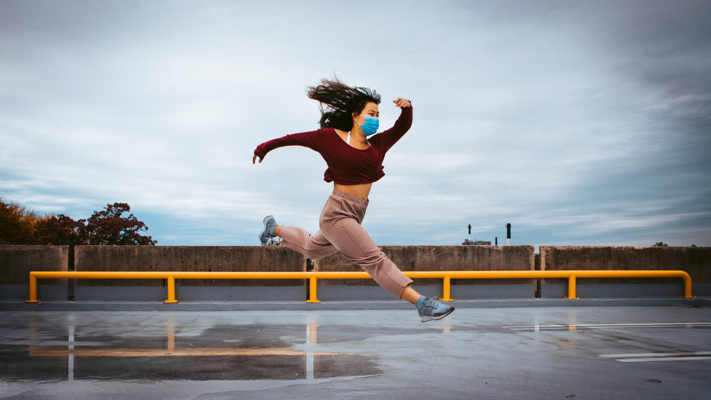Dancer wearing a face mask, jumping on the top level of a parking ramp