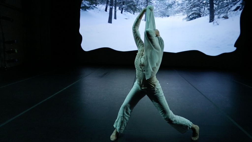 Dancer in white in front of a projection of snowy woods
