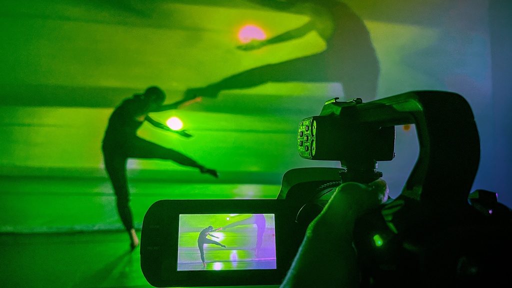 Image of dance being filmed through a camera, with their image projected behind them.