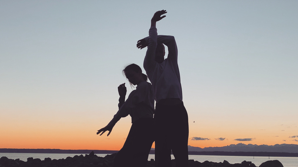 two dancers silhouetted against a sunset, on a beach