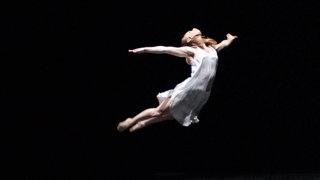 a white-clad dancer sailing through the air against a black background