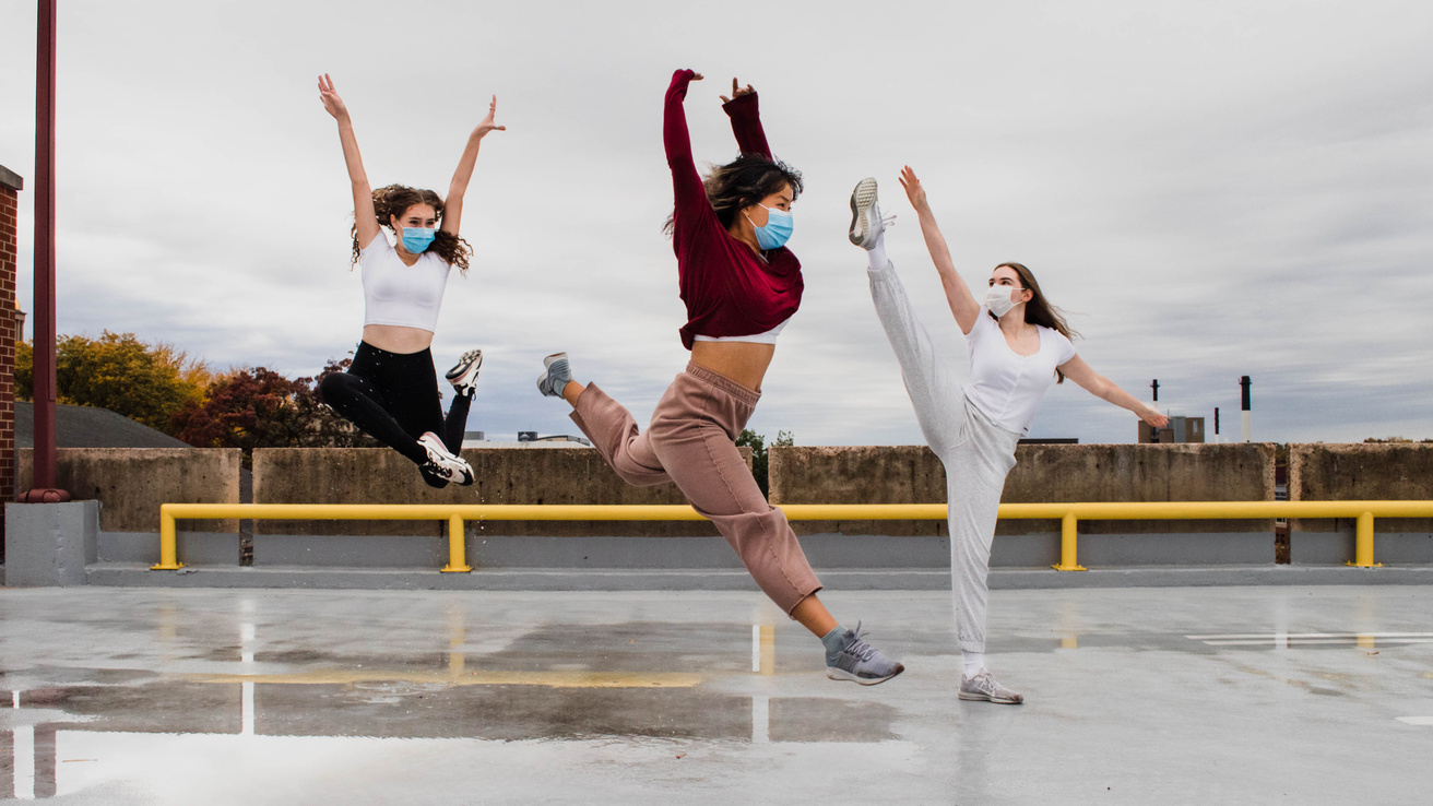 three dancers wearing face masks dance in a parking ramp